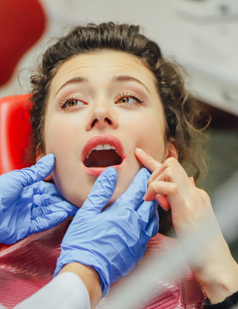 Young woman smiling in dental chair while dentist in blue gloves works on her teeth