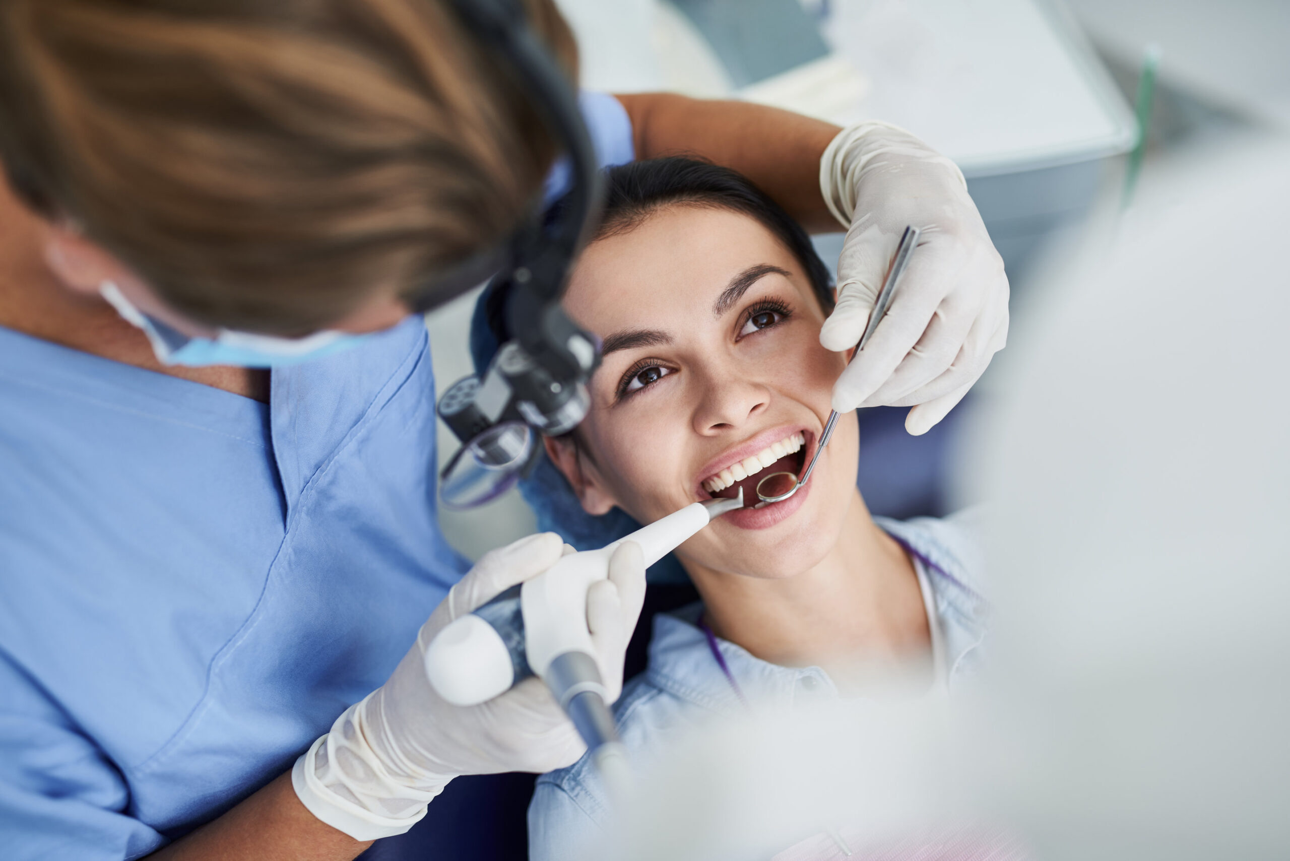 Top view portrait of beautiful lady with opened mouth sitting in dentist chair while stomatologist in sterile gloves doing professional teeth cleaning