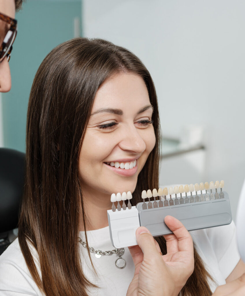 Young man dentist in white coat show veneers enamel color palette for beautiful patient woman
